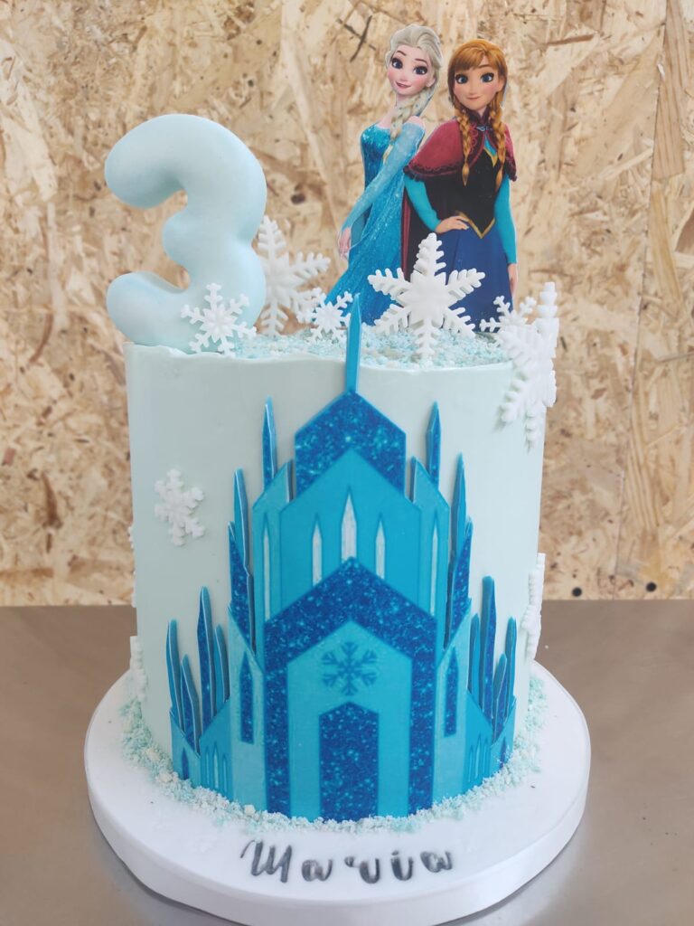 Tartas personalizadas en Madrid – diseño artesanal infantil de Frozen con figuras de Anna y Elsa, castillo de hielo en fondant y decoración azul y blanca