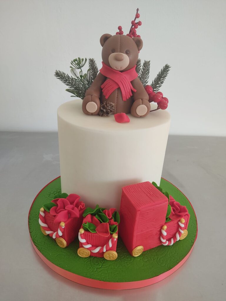 Tarta de fondant con figura 3D de oso navideño y regalos rojos, decoración artesanal ideal para Navidad.