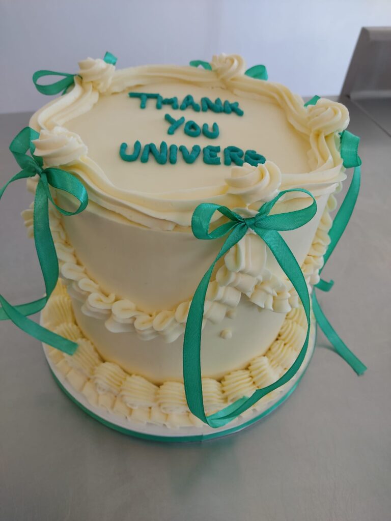 Tarta de ganache blanca decorada con lazos verdes y mensaje Thank You Universe