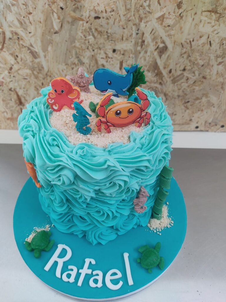 Tarta infantil azul decorada con crema y temática marina personalizada con el nombre Rafael.